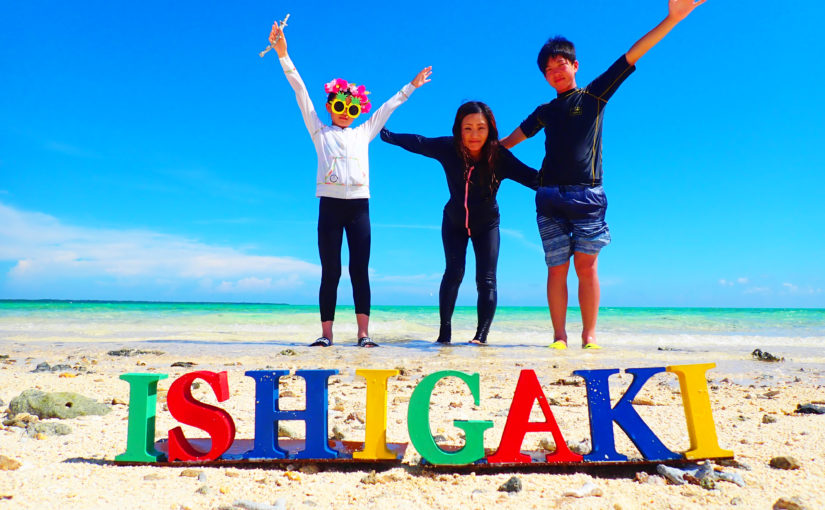 石垣島1泊2日旅行の記念写真。カラフルな「ISHIGAKI」のロゴと、晴天のビーチで楽しむ家族。