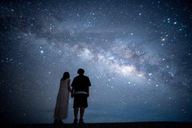 デートに人気の石垣島星空スポット。天の川の下で手を繋ぐカップルのロマンチックな写真。
