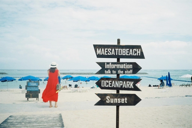 石垣島の人気観光スポット「マエサトビーチ」。リゾート感あふれる案内看板と青いパラソルが並ぶ砂浜。