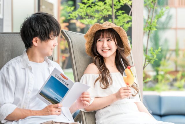 石垣島2泊3日の旅行プランを計画中。ガイドブックとトロピカルドリンクを楽しむカップル。