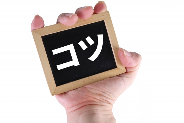 「コツ」と書かれた小さな黒板を、左手で持っている人。